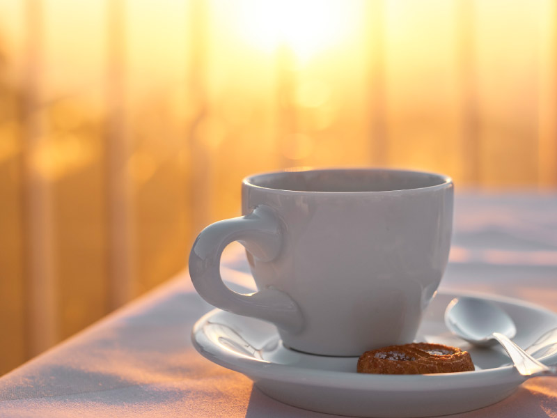 Weiße Kaffeetasse auf Tisch von Sonne angeleuchtet
