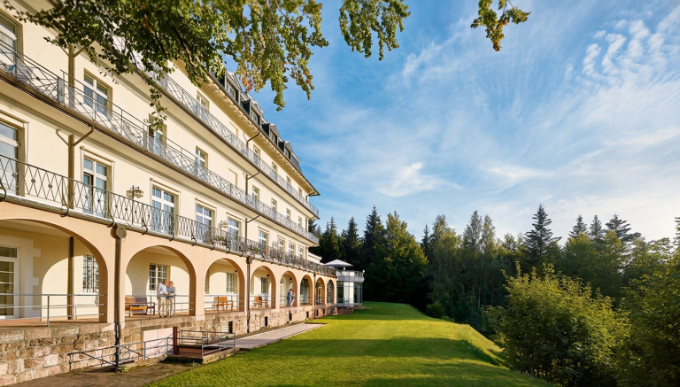 Großzügige Außenansicht der Max Grundig Klinik mit Arkaden, Balkonen und weitläufigem Garten am Waldrand