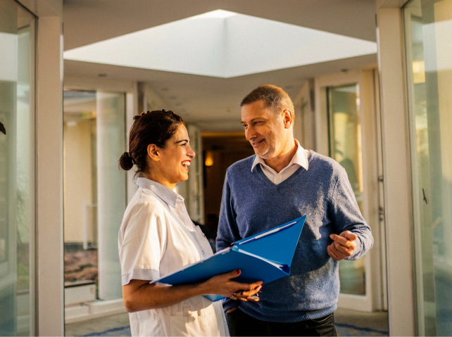 Eine Mitarbeiterin der Klinik 
spricht mit einem Patienten auf dem Flur