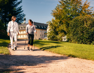 Frau läuft mit Walking Stöcken im Park vor der Klinik