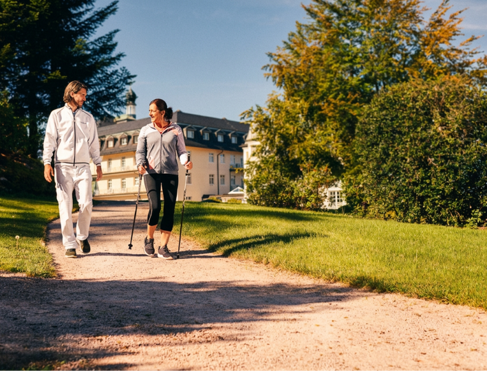 Frau läuft mit Walking Stöcken im Park vor der Klinik