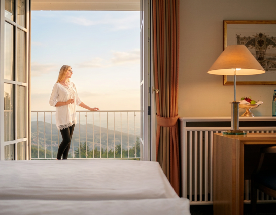 Zimmer mit Balkon und Panoramablick, eine Frau genießt die Aussicht in ruhiger Atmosphäre